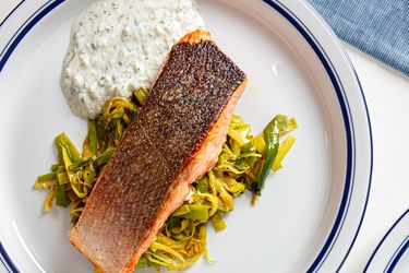 A plated dish of salmon with a crispy skin on a bed of leeks accompanied by a serving of sauce on the side