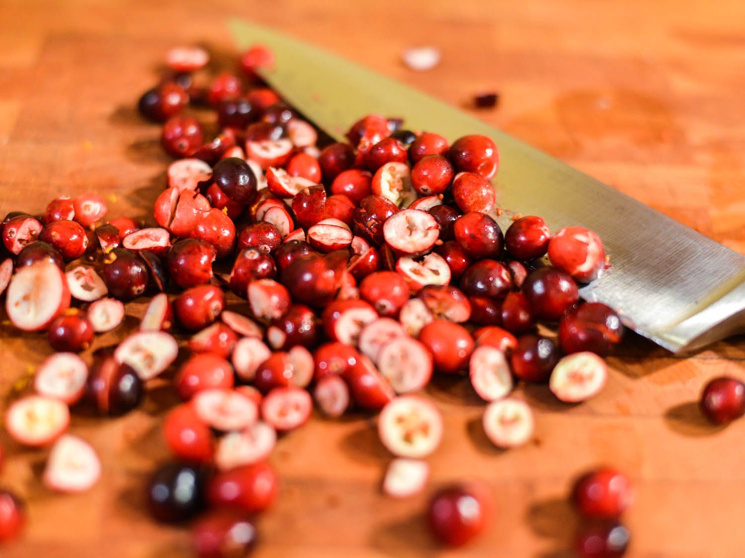 Knife-chopped fresh cranberries on a wooden cutting board.