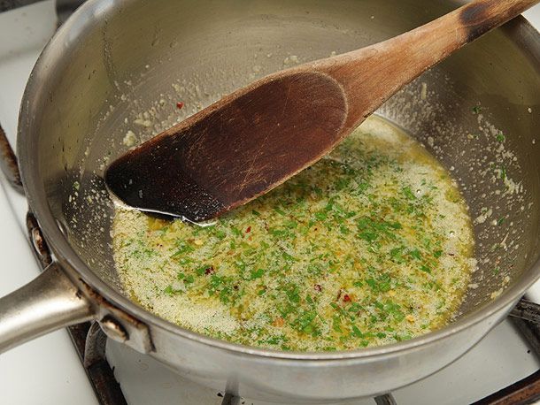 A wooden spoon stirring melted butter and herbs in a saucepan on the stove