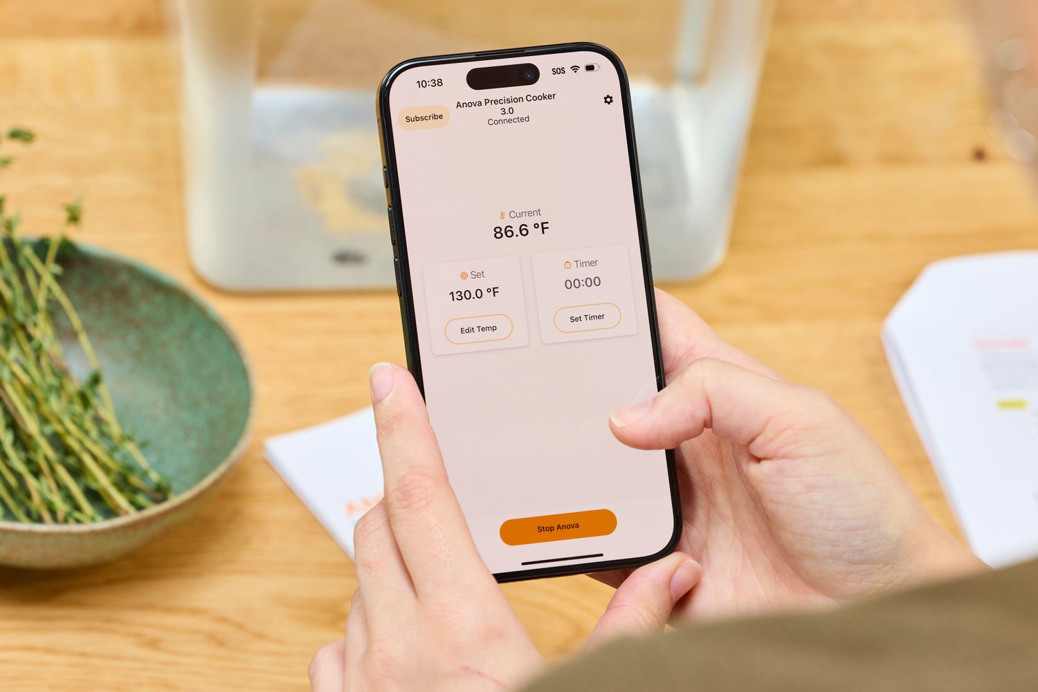Person holding a smartphone displaying a cooking app interface for the Anova Culinary Precision Cooker 3.0 with temperature settings visible