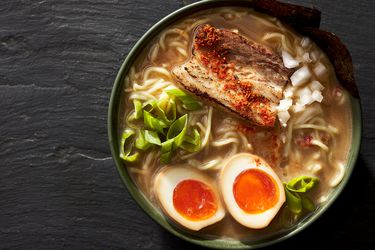 Bowl of ramen garnished with meat, eggs, and green onions on a black stone surface 