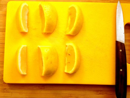 Six lemon wedges resting on a cutting board.