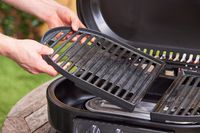 A person sets grill grates inside a portable gas grill.