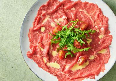 beef carpaccio garnished with tomato quarters and baby arugula