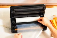 A person using the Anova Precision Pro vacuum sealer's built-in bag cutter to trim a bag off of a roll.