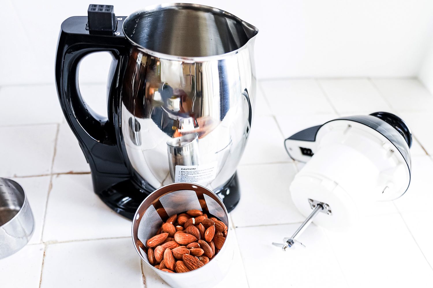 Kitchen appliance including a metal blender or mixer bowl with attached components and a small container of almonds