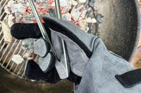 A person holds a pair of tongs while wearing the Breeo Fire Pit Gloves