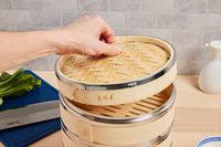 a person lifting the lid on a bamboo steamer