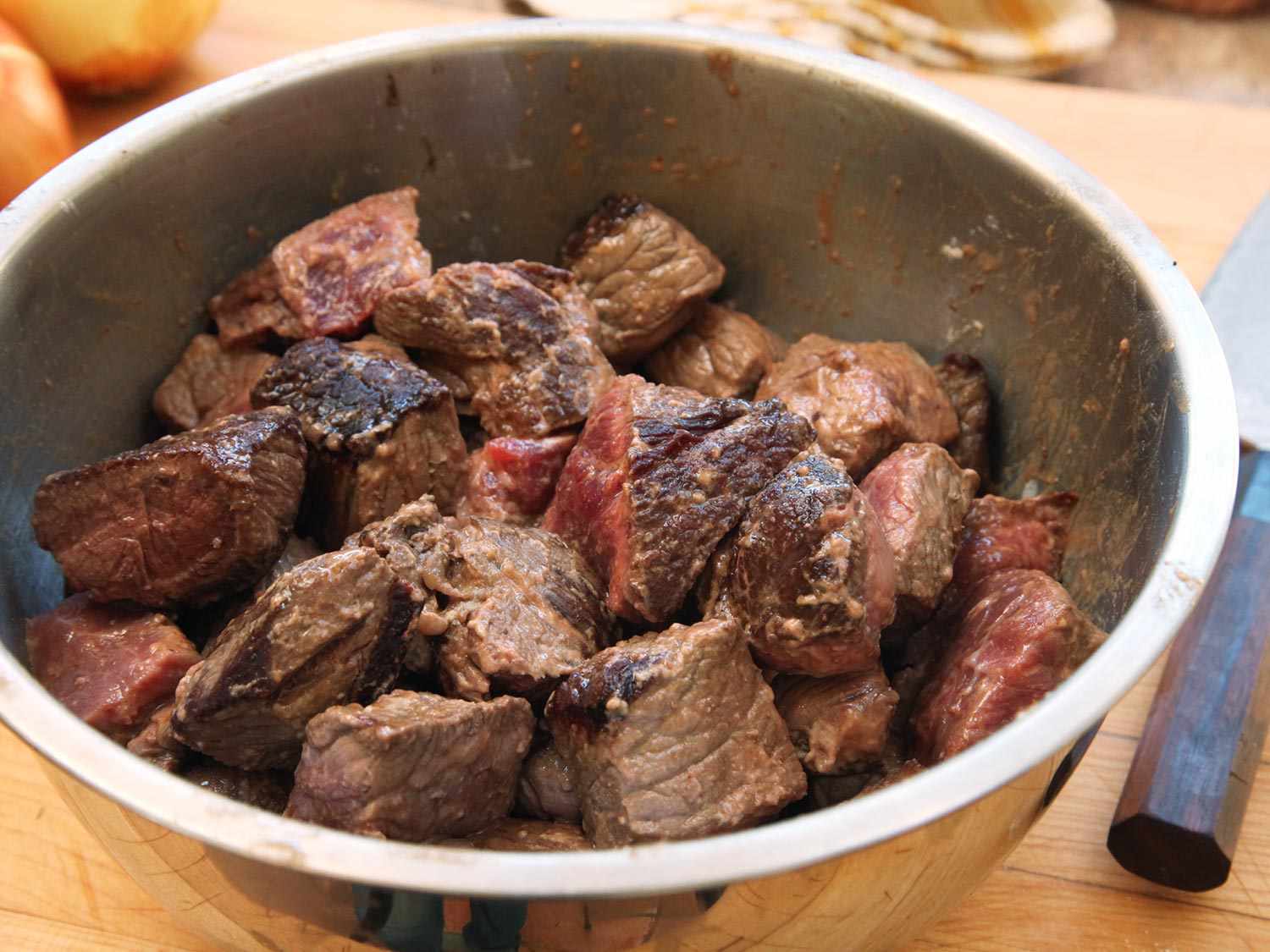 Browned beef chuck pieces coated in flour in a large metal mixing bowl.