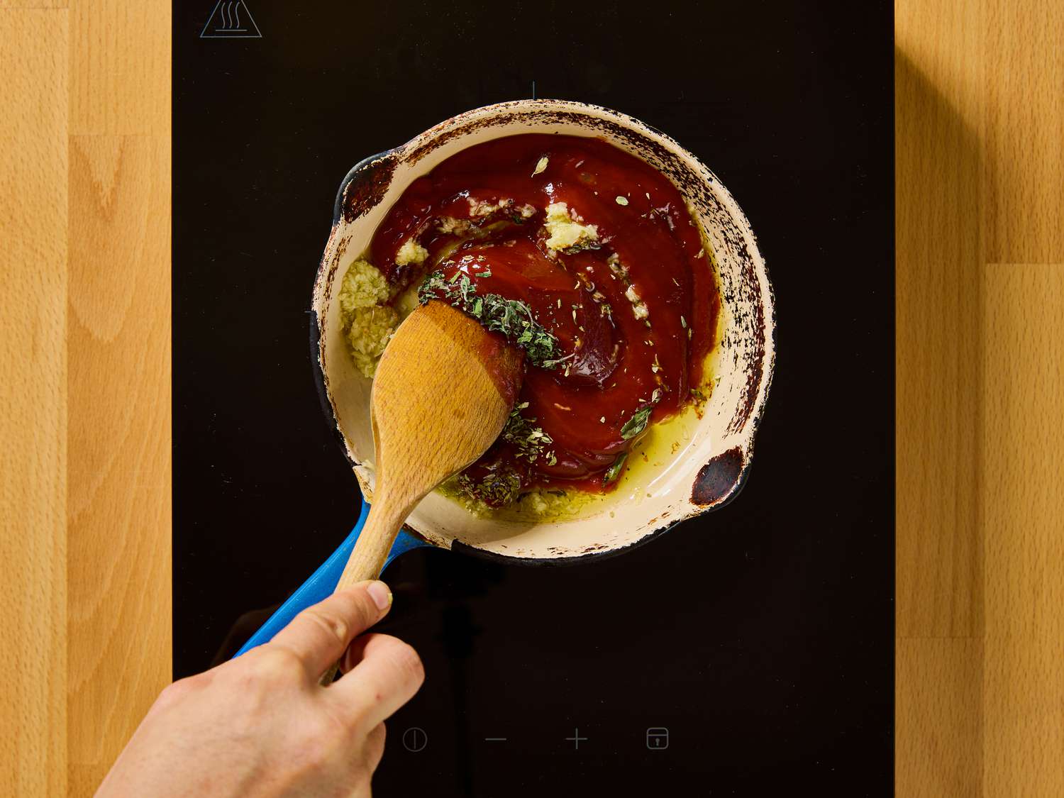 A hand stirring sauce ingredients in a pan on a stovetop
