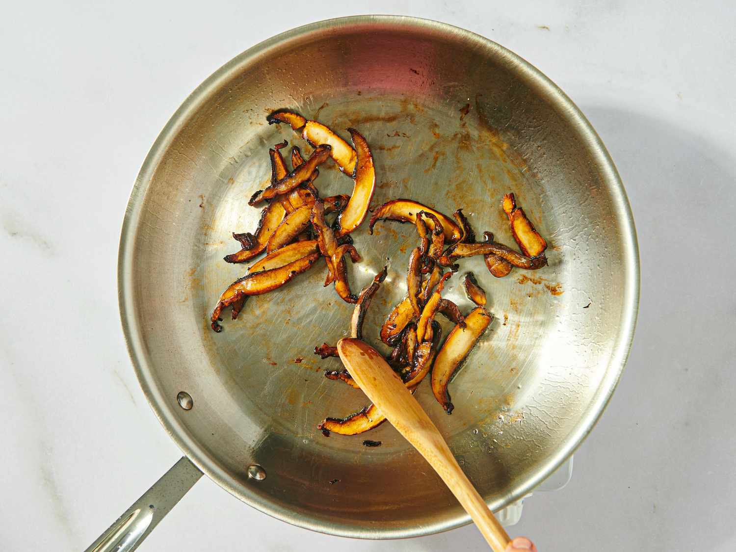 Sautéed mushrooms in a frying pan being stirred with a wooden spoon