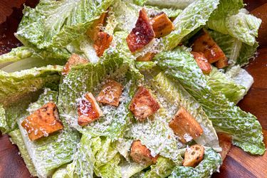 A Caesar salad with romaine lettuce croutons grated cheese served in a wooden bowl