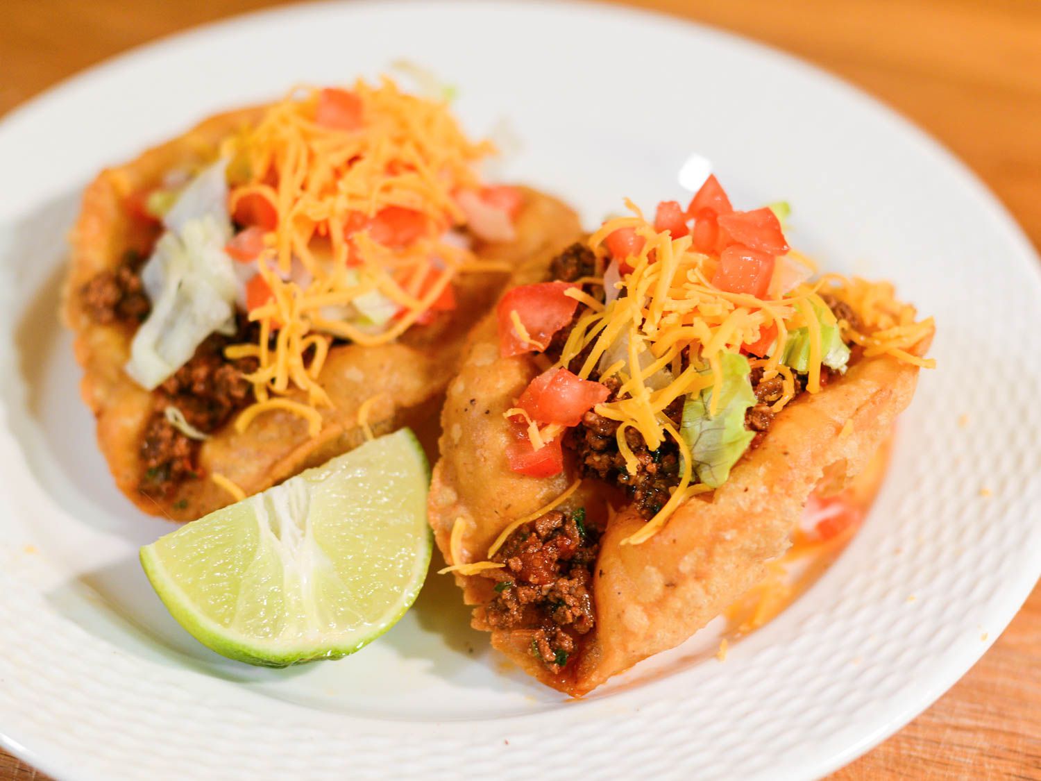 Two San Antonio-style puffy tacos filled with spiced beef and topped with cheese.
