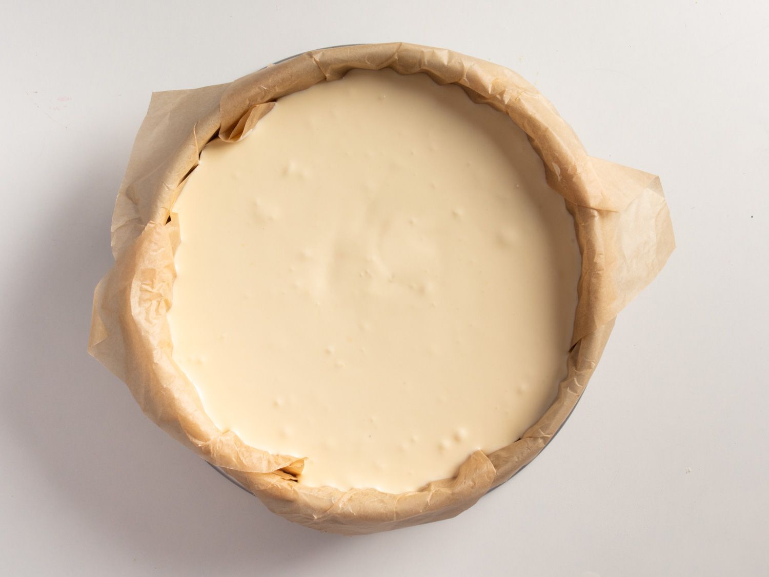 Overhead of the cheesecake batter resting in a parchment paper lined springform cake pan.