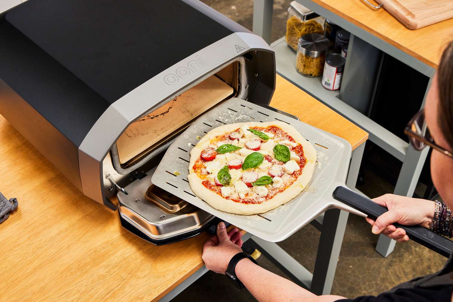 A person places a pizza into the Ooni Volt 12 Electric Pizza Oven to cook
