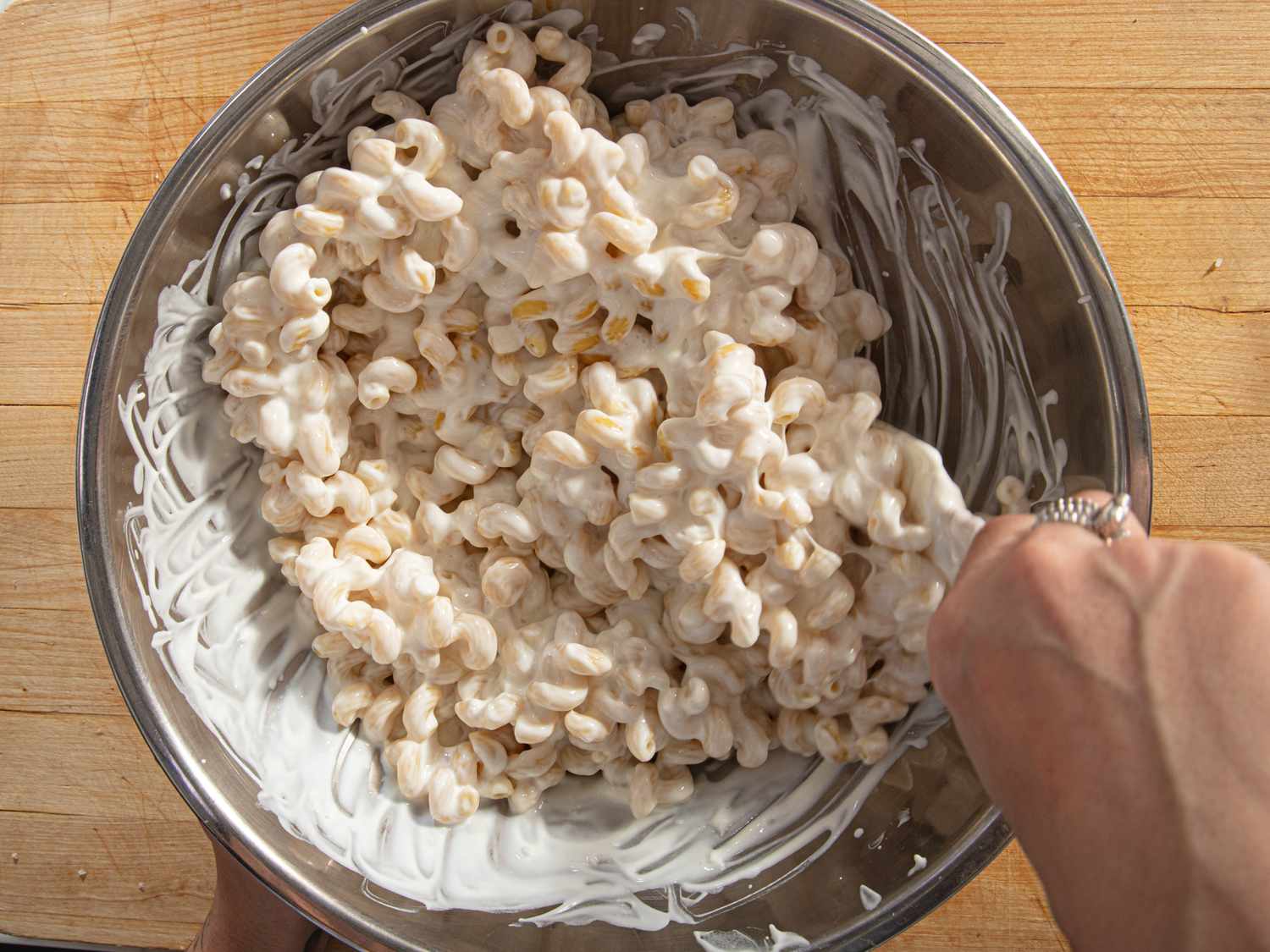 A hand stirring a bowl of pasta coated in a creamy sauce