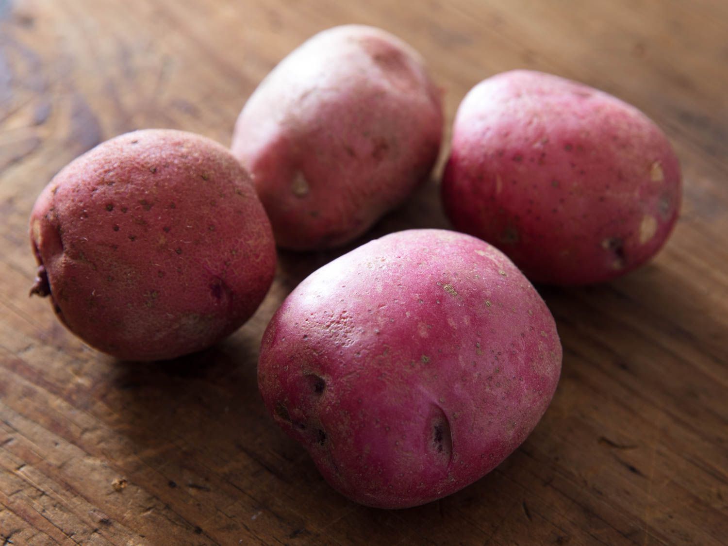 Four red-skinned potatoes on a wooden cutting board.