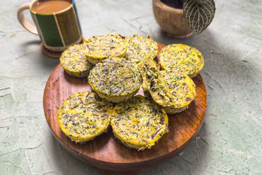 Wooden platter of egg bites, with one cut open. On a stone surface, with coffee and a small plant in the background
