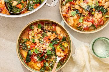 Bowls of soup with white beans tomatoes and collard greens on a table setting