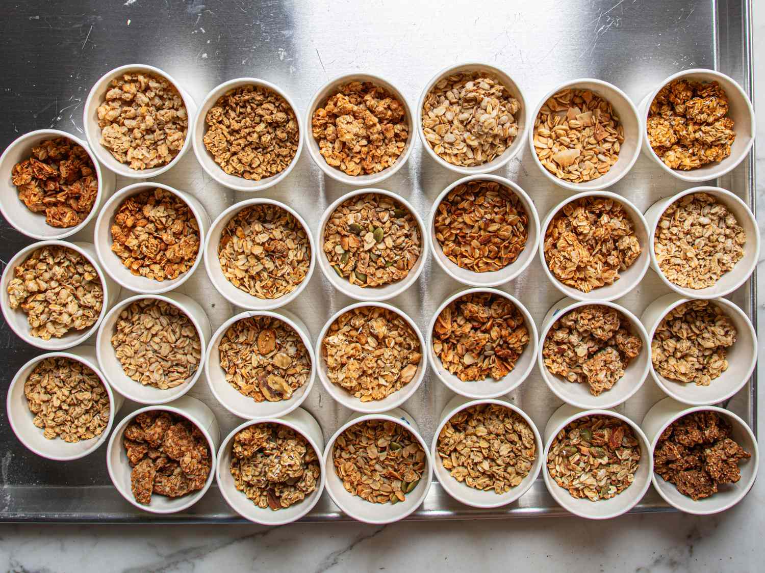 A collection of bowls filled with various granola types arranged on a tray