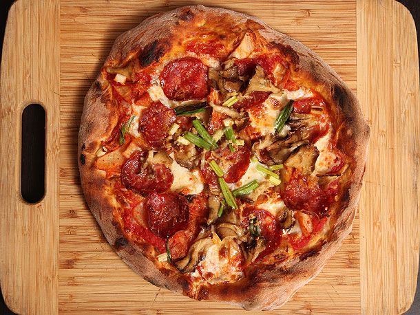 New York-style pizza with kimchi, soppressata, and maitake mushrooms on wooden board