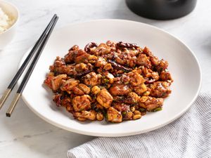 A plate of real-deal kung pao chicken with chopsticks on the side of the plate. 