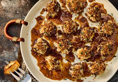 Plate of baked appetizers topped with breadcrumbs and a fork with a slice of bread on a table