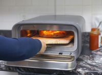 a person removing a pizza from an indoor pizza oven