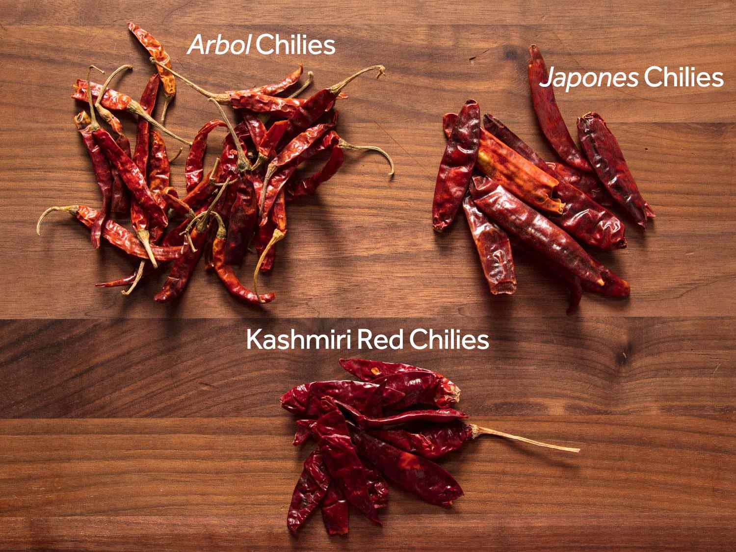 Dried árbol, japones, and Kashmiri red chilies on a wooden surface.