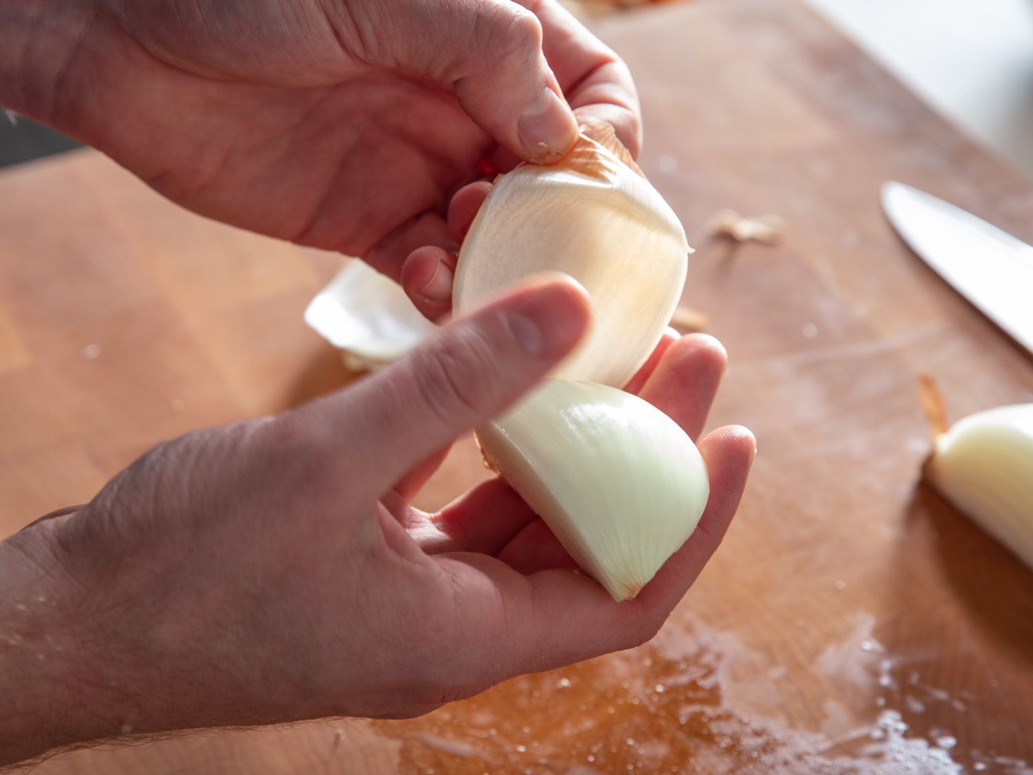 Peeling off skin and papery layer underneath on a quarter onion.