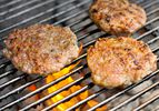 Three breakfast sausage patties cooking on a grill. 