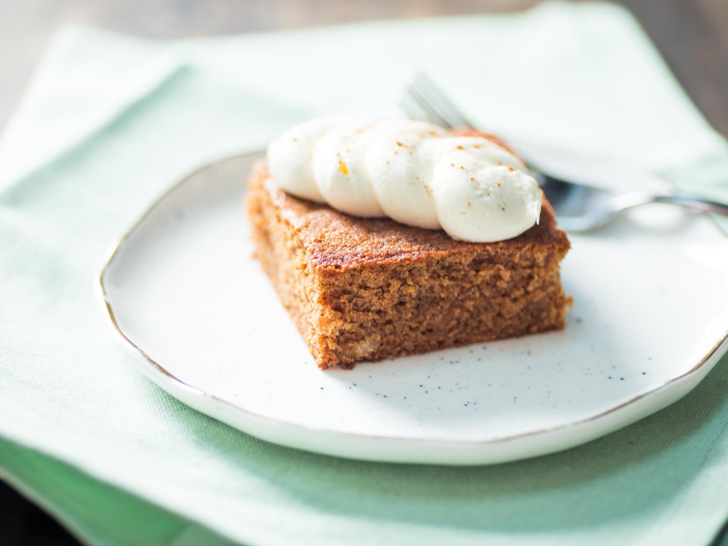 A slice of gingerbread cake, topped with wavy frosting, on a speckled ceramic plate.