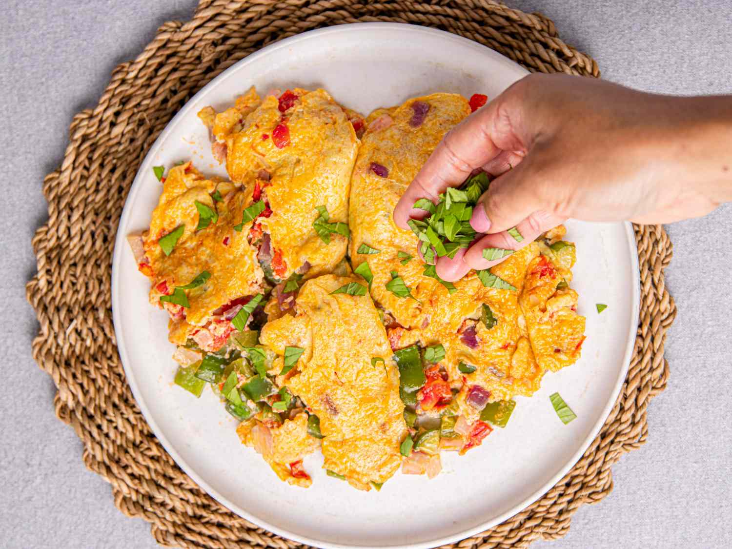 A plate of Nigerian omelet garnished with green onions with a hand placing some green onions on top