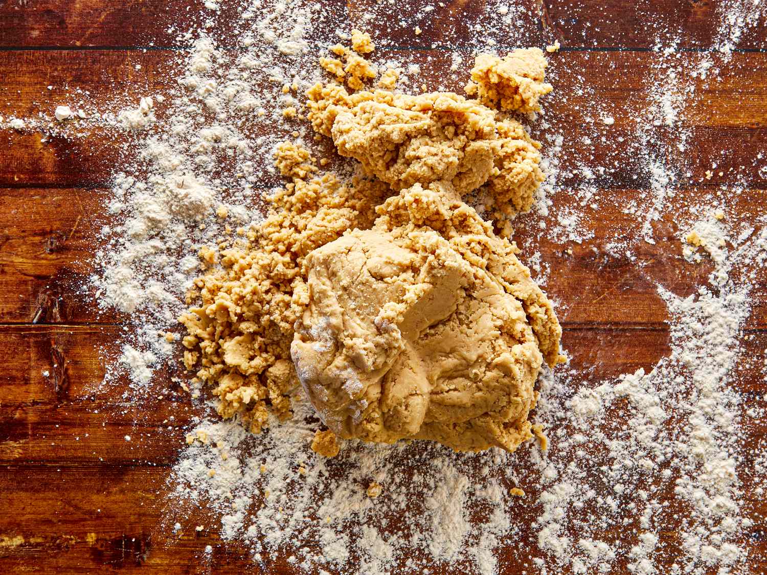 A ball of dough and flour scattered on a wooden surface