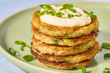 stack of boxty pancakes with dollop on sourcream, and garnished with green onions on a green place on stone surface.