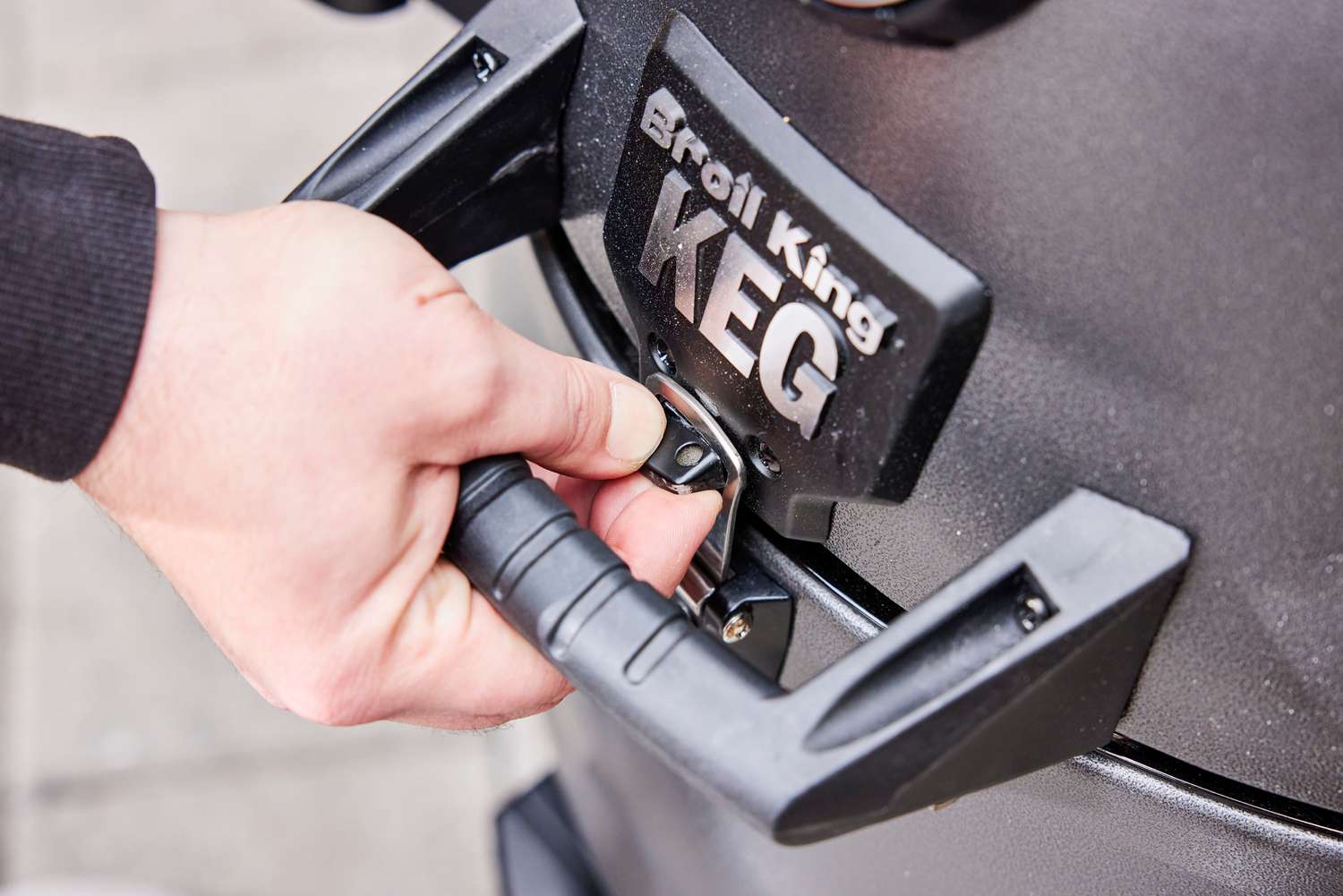 A person unlocks the Broil King Keg Kamado Charcoal Grill