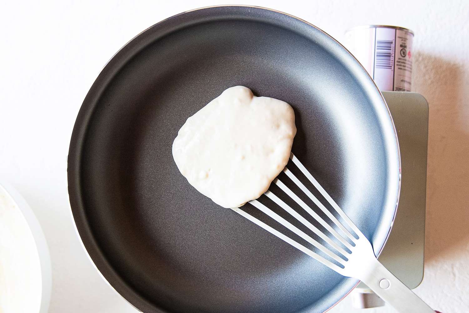 A metal fish spatula flipping a pancake in a frying pan