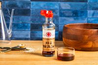 A bottle of pure sesame oil on a kitchen counter with utensils, bowl, and glass nearby