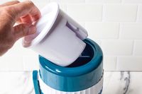 A hand lifting a white plastic component from MANBA Ice Shaver and Snow Cone Machine