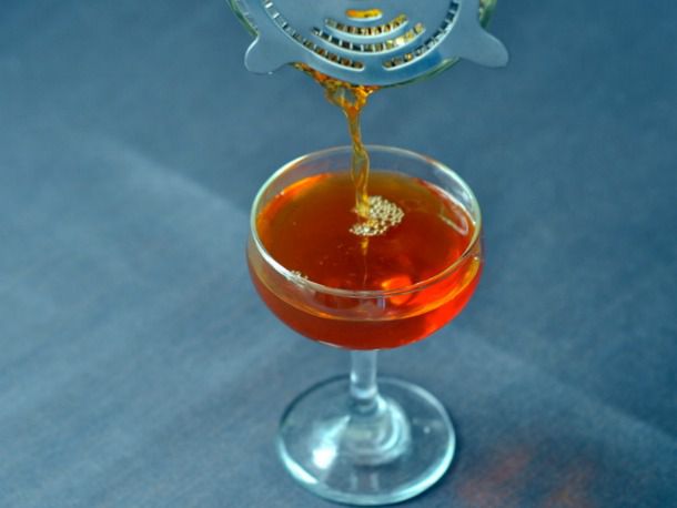 A Fanciulli cocktail being strained and poured into a coupe from a cocktail shaker.