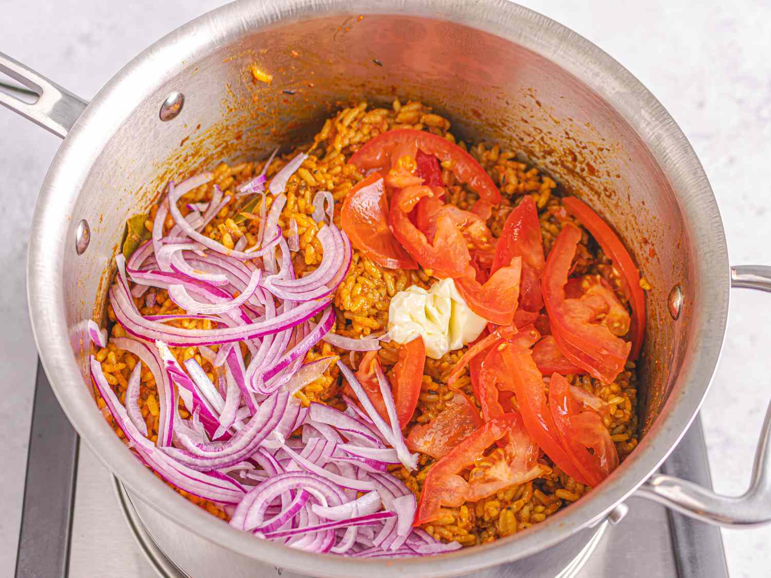 Overhead view of tomatoes, onions and butter added to rice