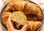A plate of croissants with a hand holding a halved croissant showing its layers
