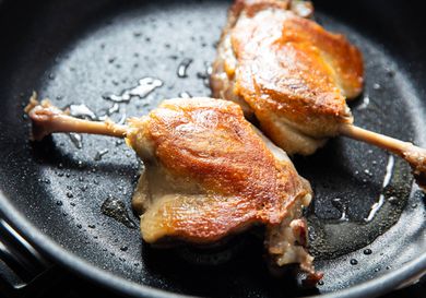 Two duck confit legs in a skillet. 