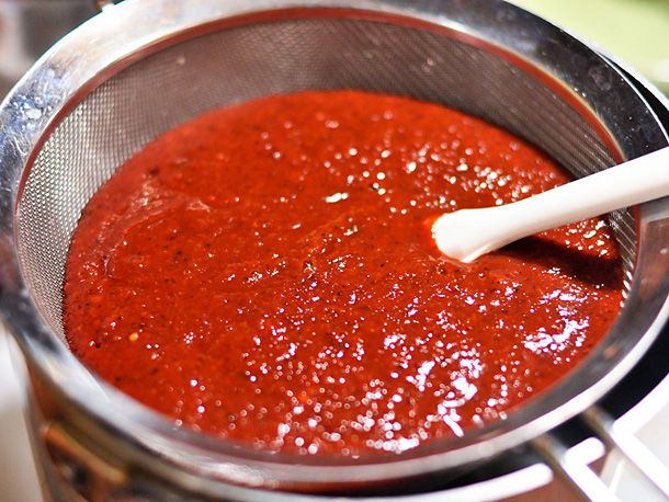 Pressing homemade red enchilada sauce through a fine-mesh strainer.