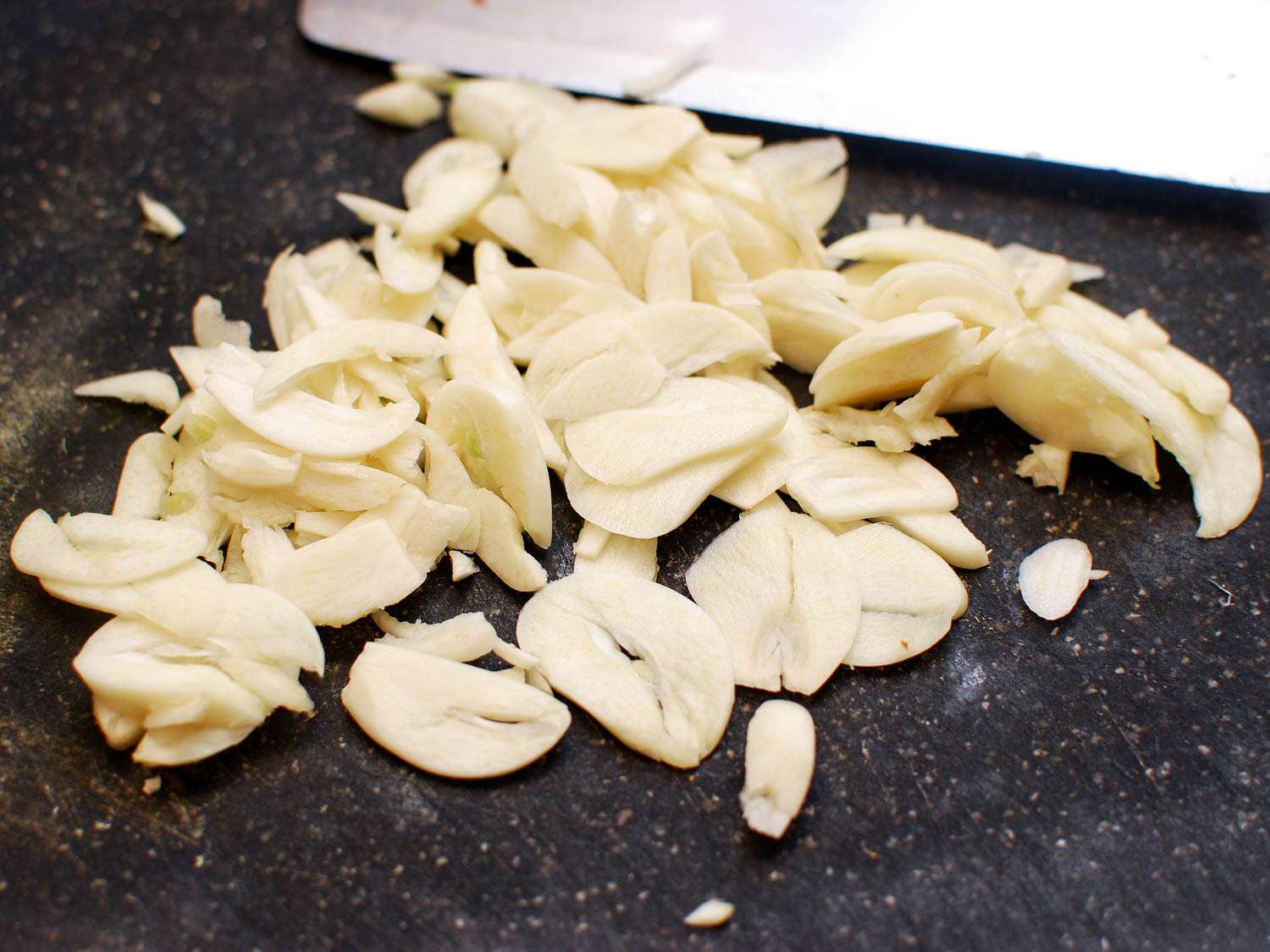 A pile of sliced garlic on a cutting board, ready to add to the wok.