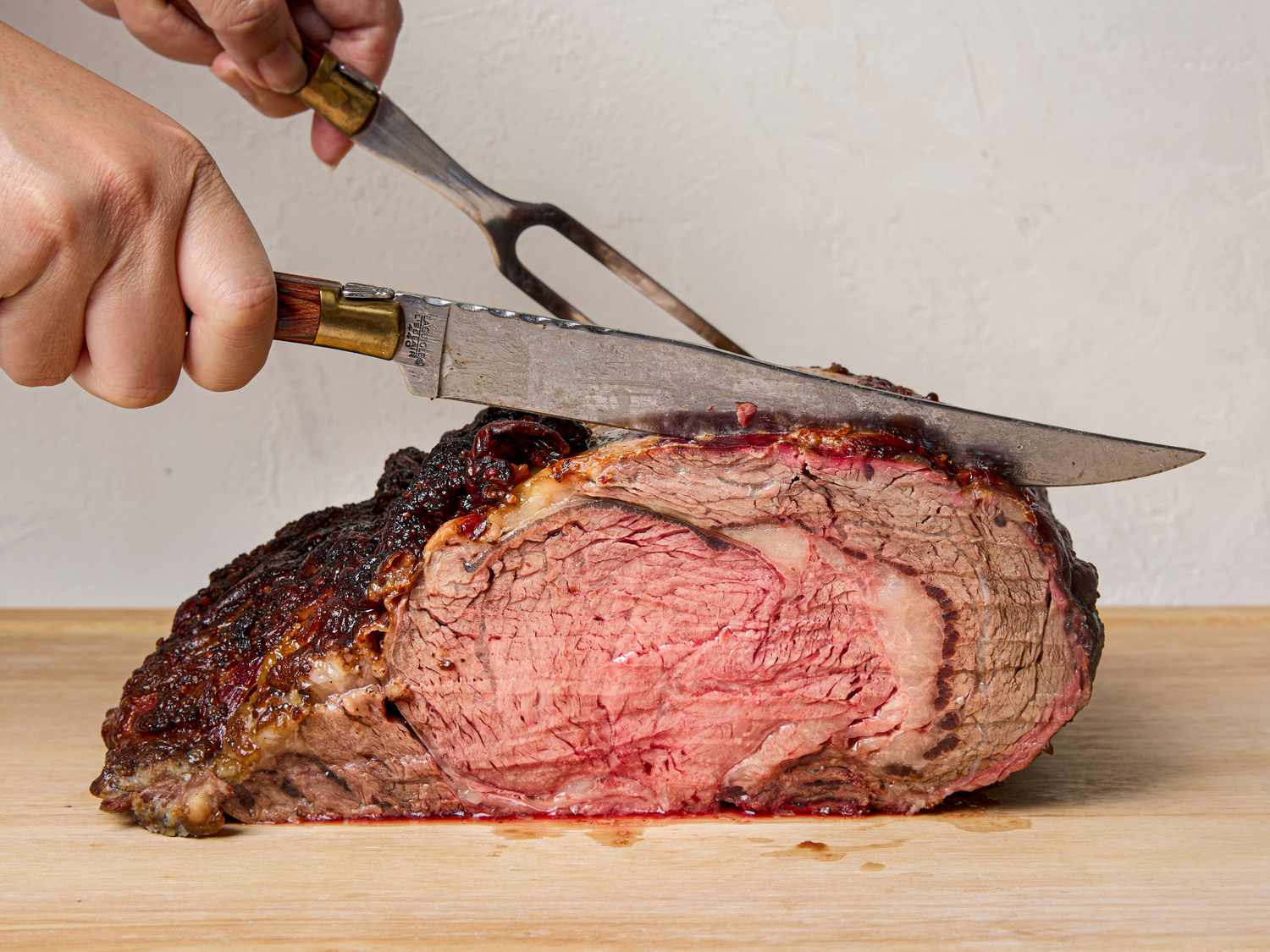A cooked prime rib roast being carved with a knife and fork on a cutting board