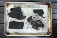 Pieces of charcoal arranged on a metal tray with a ruler