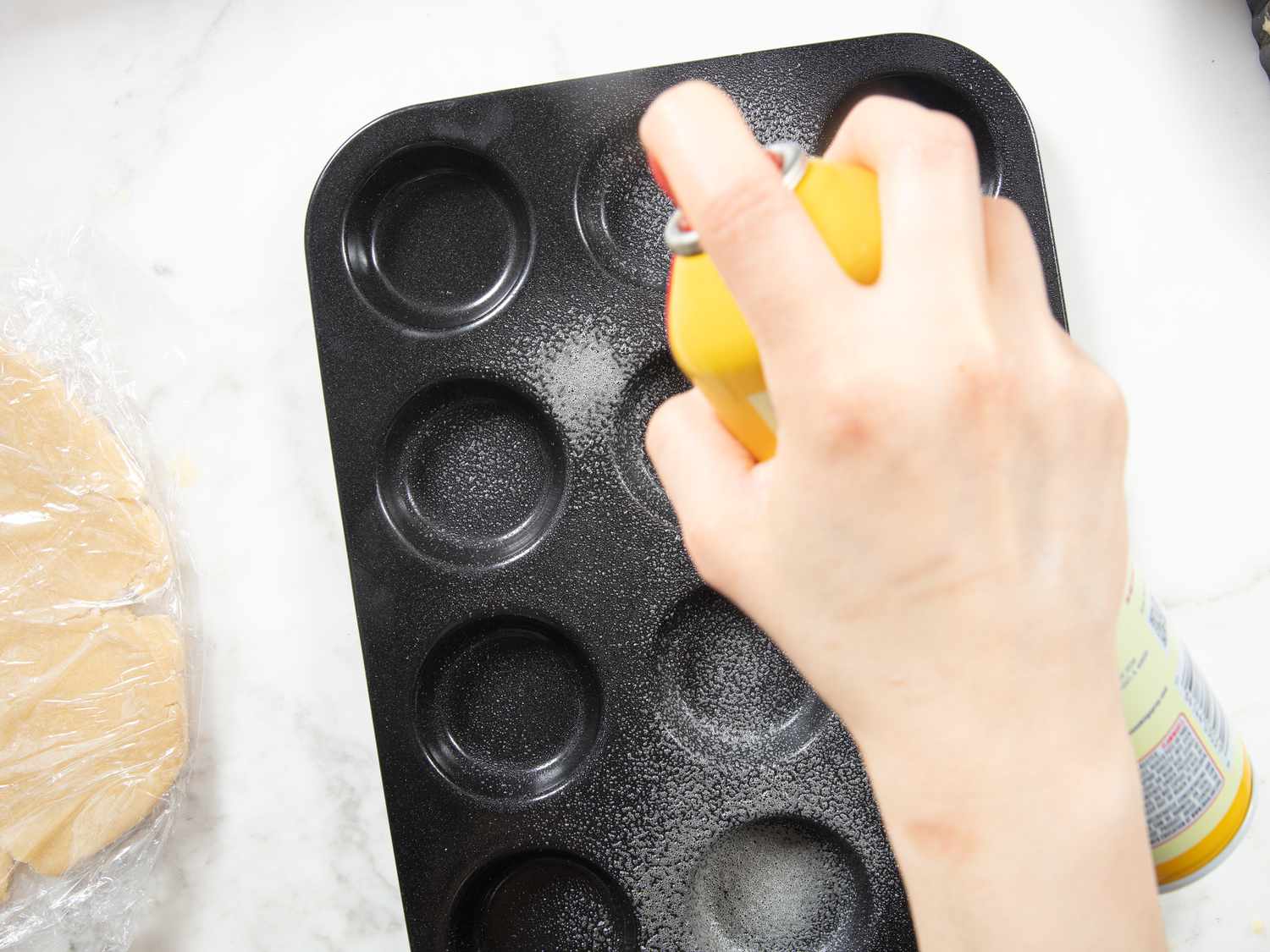 spraying a muffin tin on a wite marble surface