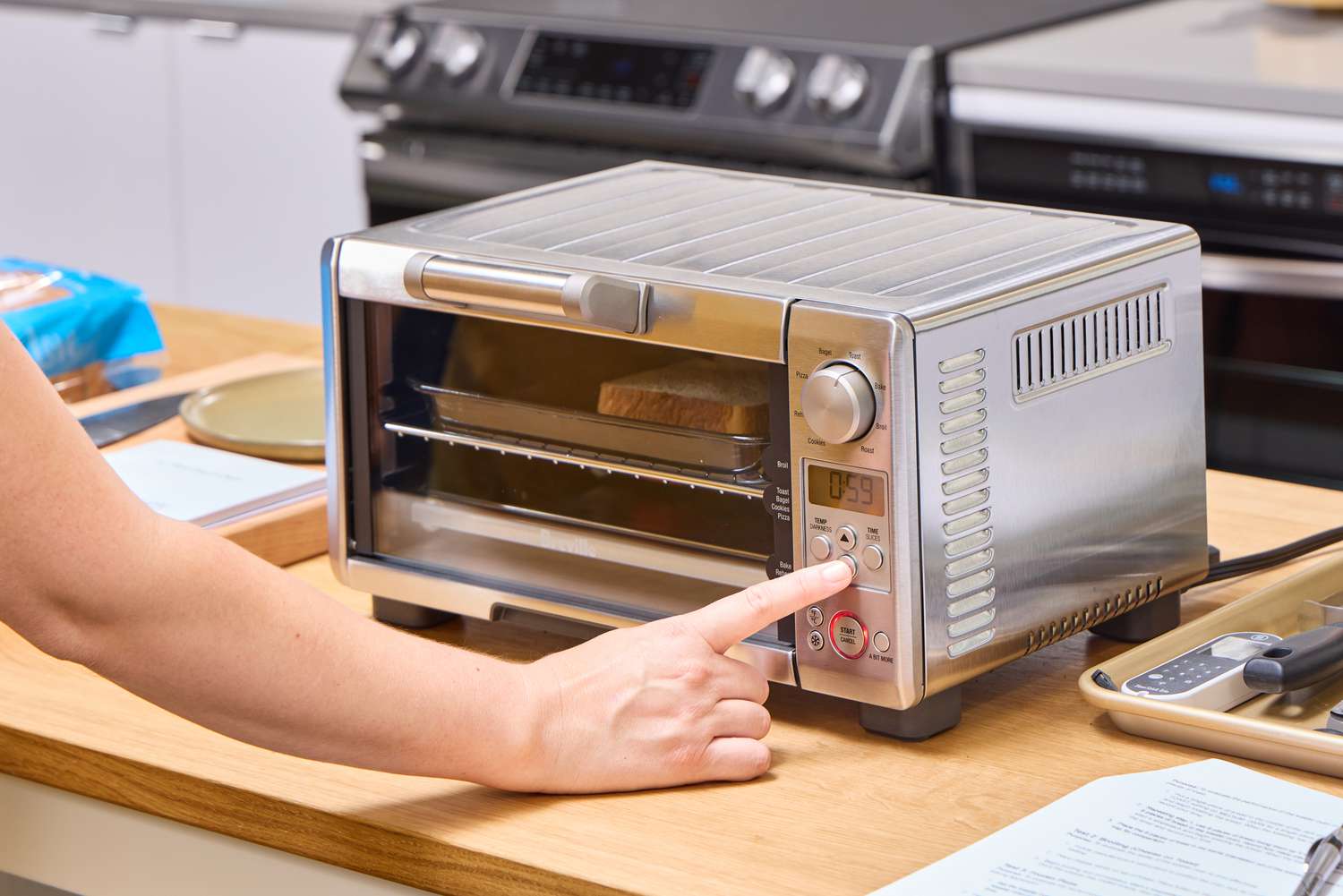 A finger pressing a button on the Breville the Mini Smart Oven BOV450XL