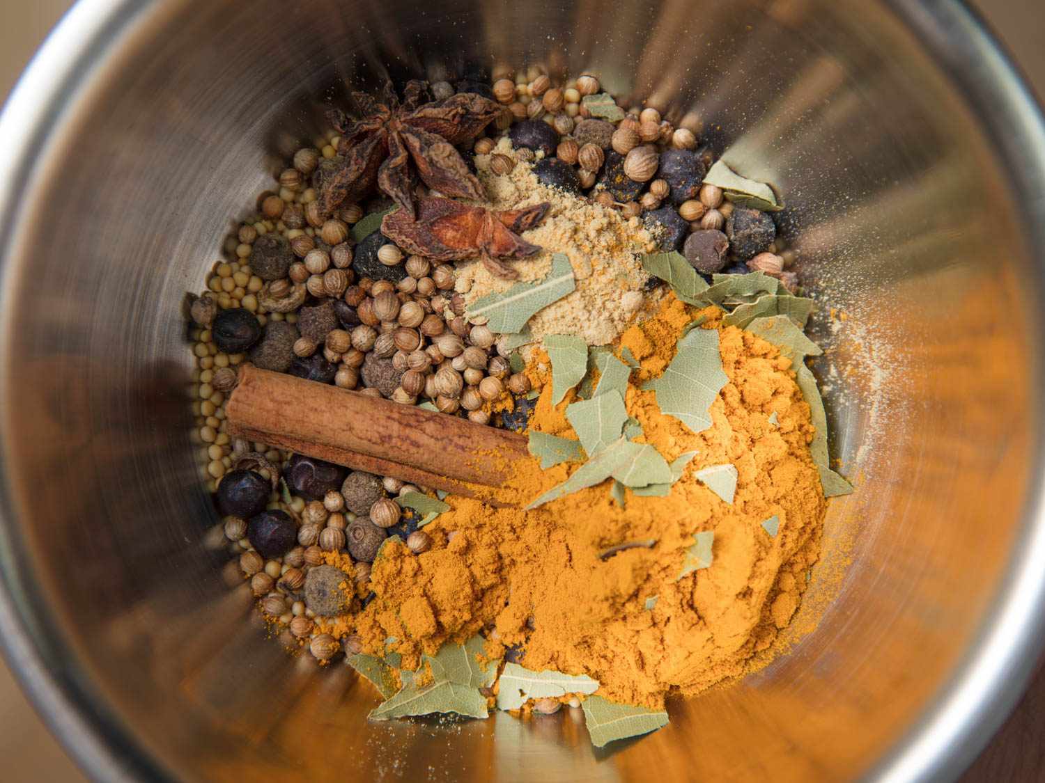 Overhead view of bowl filled with spices for flavoring homemade pickles: cloves, allspice, mace, anise, juniper, and loads of mustard seed and turmeric